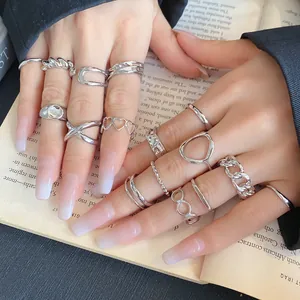 Detailed view of assorted silver geometric open rings on hands resting on a book