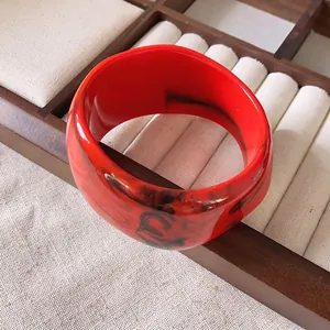 Vista dettagliata di un ampio bracciale irregolare in resina rossa con motivi marmorizzati neri