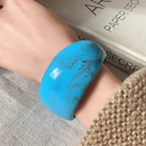 Dettaglio di un bracciale rigido in resina blu marmorizzato indossato, design moderno.