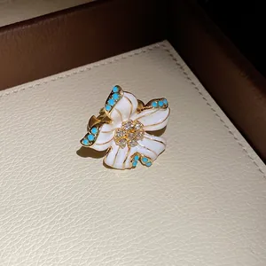 Close-up of a vintage-style white enamel flower pendant with rhinestones and turquoise accents