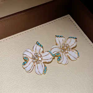 Detailed macro view of a white enamel flower pendant with crystal center and blue beads.
