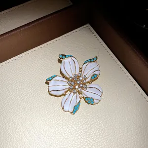 Close-up of elegant white enamel flower brooch with blue beads and crystals.