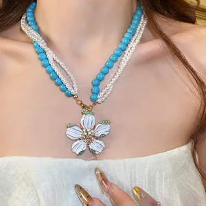 Detail view of a vintage multi-strand turquoise and pearl necklace with enamel flower pendant.