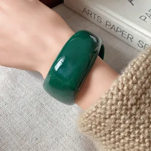 Dettaglio di un ampio bracciale in resina marmorizzata verde scuro indossato al polso