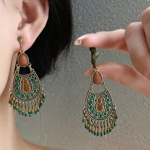 Detail view of vintage ethnic teardrop earrings with green beads and oil-drip tassels.