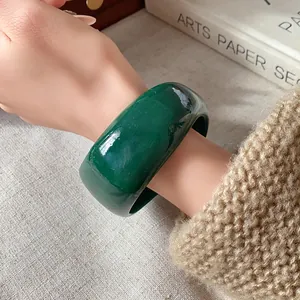 Vista dettagliata di un ampio bracciale in resina verde scuro su un polso in maglia.