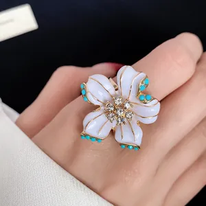 Close-up of a vintage white enamel flower ring with rhinestone center on finger