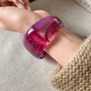 Dettaglio di un ampio bracciale in resina viola traslucida con motivo marmorizzato.