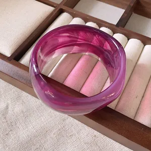 Dettaglio macro di un ampio bracciale in resina marmorizzata magenta su vassoio per gioielli