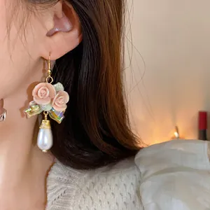 Nahaufnahme eleganter französischer Vintage-Rosen-Keramikohrringe mit Perlenanhängern am Ohr.