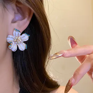 Detailed close-up showing a white enamel flower earring with a sparkling crystal center