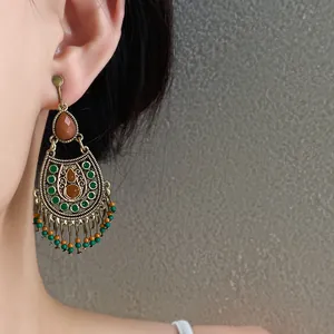 Close-up of vintage ethnic-style earrings with green drip oil and tassel beads on ear