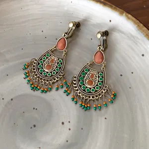 Vintage Bohemian ethnic drop earrings with green and orange bead tassels on a ceramic plate