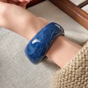 Dettaglio di un largo bracciale rigido in resina blu marmorizzata su fondo di lino neutro