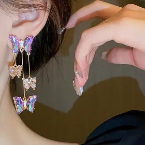 Détail des boucles d'oreilles pendantes à pompons avec papillons en zircon violet et clair.