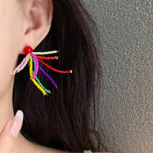 Detailansicht bunter unregelmäßiger Harzperlenohrringe mit rotem Stecker am Ohr eines Modells.
