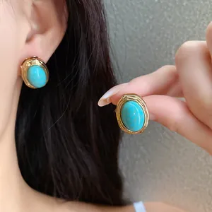 Close-up detail of vintage turquoise oval stud earrings with textured gold-tone metal frame