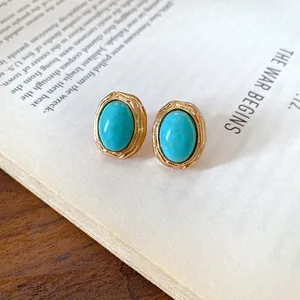 Vintage oval turquoise stud earrings with textured gold border on book page detail