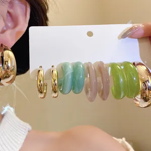 Close-up of a multi-pair earring set featuring gold-tone hoops and colorful resin C-hoops