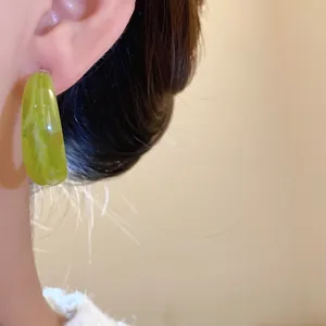 Detailed view of a retro avocado green marble pattern teardrop earring worn on a model's ear