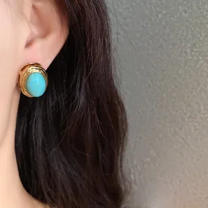 Close-up view of a vintage gold-toned earring featuring a turquoise stone on ear