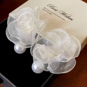 Macro detail shot of elegant white mesh flower earrings with smooth artificial pearls