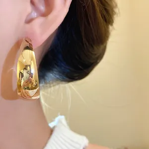 Close-up of a glossy gold water drop hoop earring on an ear, minimalist retro style