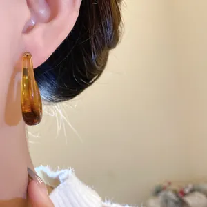 Detailed close-up of vintage amber water drop earrings with silver needles on ear