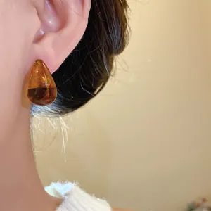 Close-up detail of an amber teardrop stud earring showing the smooth resin texture