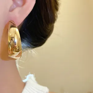 Detail shot of a minimalist chunky gold waterdrop hoop earring worn by a model