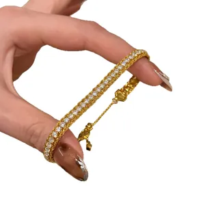 Elegant gold zircon adjustable bracelet held between fingers on white background.