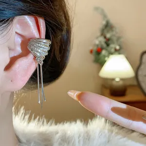 Detalle de un ear cuff plateado minimalista con capas de circón y borlas largas colgantes.
