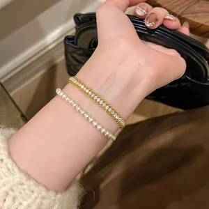 Close-up of elegant gold zircon bracelet and delicate pearl strand worn on woman's wrist