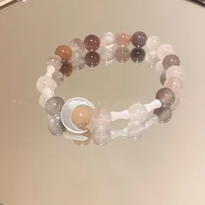 Detail view of crystal bead bracelet with crescent moon charm on a mirror surface