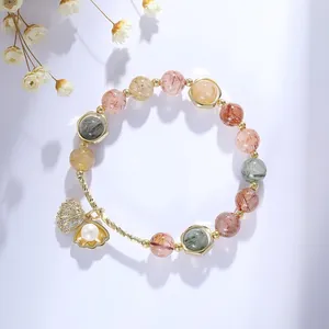Detailed view of a rutilated quartz bead bracelet with a golden shell and pearl charm.