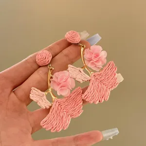 Close-up of pink raffia flower earrings showing intricate woven leaf details.
