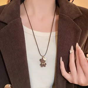 Dettaglio collana con orsetto floccato marrone e fiocco su cordino di cuoio.