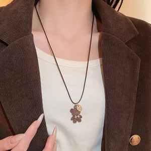 Dettaglio ravvicinato di una collana con orsetto floccato marrone e fiocco su cordino