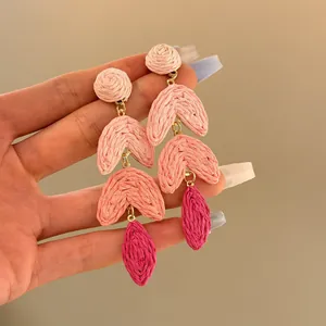 Close-up of pink raffia flower drop earrings held by hand for detail and scale