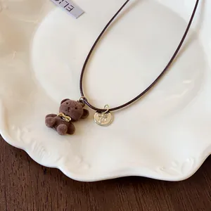 Dettaglio di una collana con orsetto floccato marrone con ciondolo a fiocco e cordino scuro