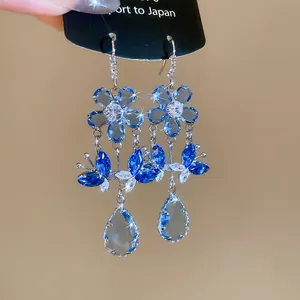 Close-up detail of luxury blue zircon dangling earrings with flower and butterfly charms