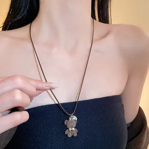 Primo piano di una collana con ciondolo a forma di orsetto floccato marrone e fiocco dorato