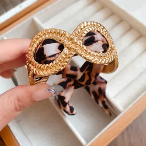 Close-up of gold alloy infinity bracelet with leopard print silk ribbon detail