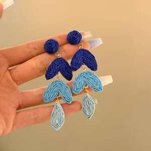 Close-up view of handmade blue raffia woven tiered flower drop earrings held in hand