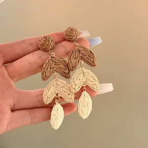 Detail view of multi-tiered raffia earrings featuring hand-woven brown and cream textures.