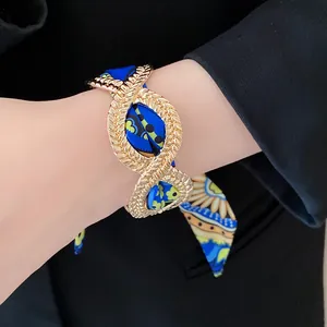 Close-up of a French style gold alloy bangle with a blue patterned silk scarf ribbon.