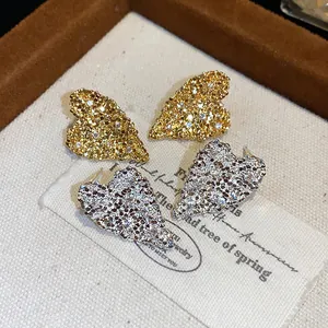 Dettaglio di orecchini a lobo a forma di cuore strutturato oro e argento con zirconi