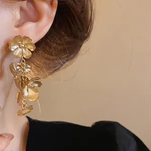 Boucles d'oreilles pendantes à fleurs en or mat de style vintage portées par un mannequin