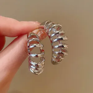 Close-up of chunky silver geometric hoop earrings with polished metallic ribbed design.