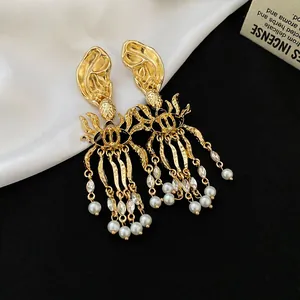 Close-up of gold geometric earrings with pearl and rhinestone tassels on a black background